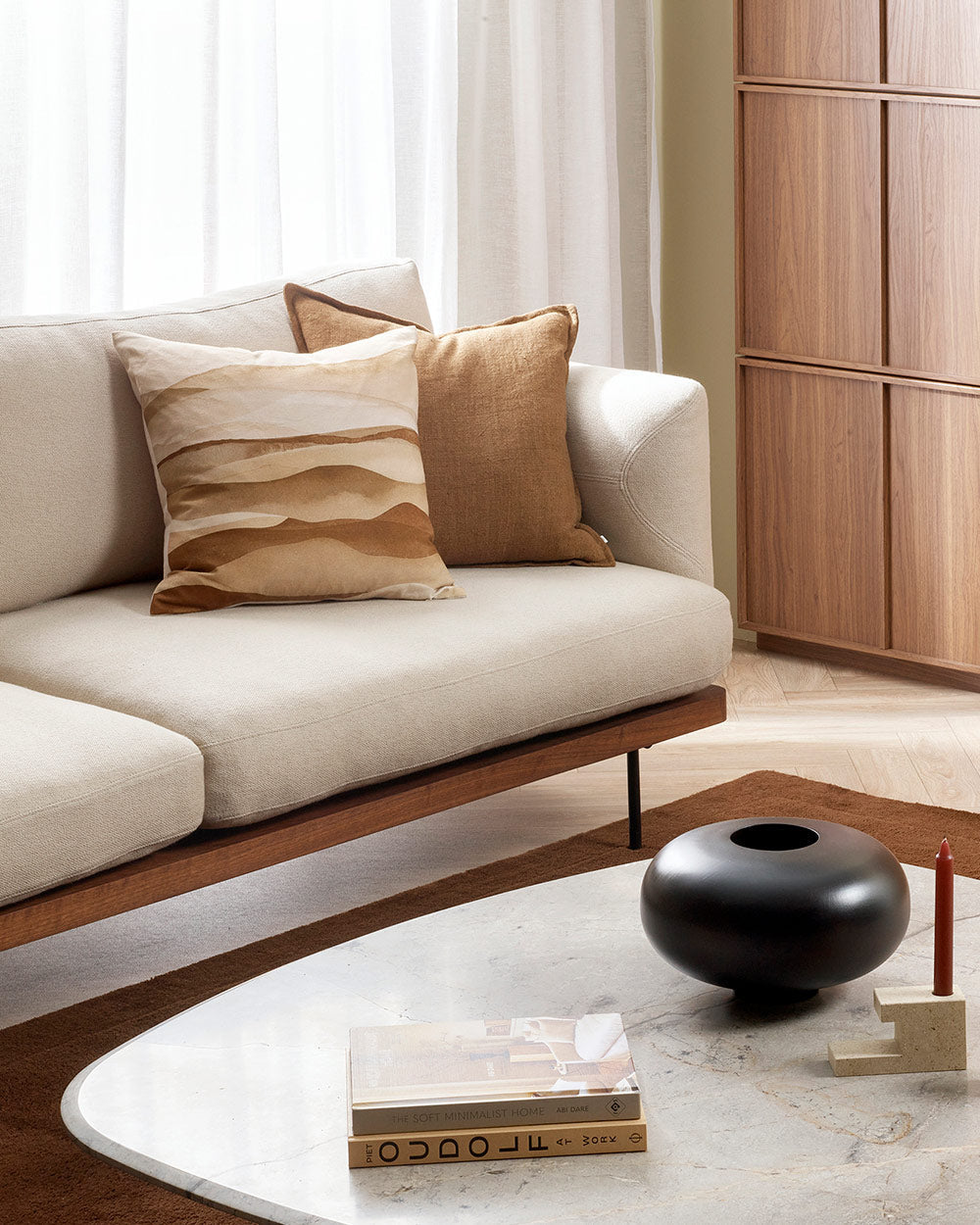 The corner of a couch and a coffee table, with a gorgeous feature cushion showcasing fine cotton printing with warm brown pigments. By Baya