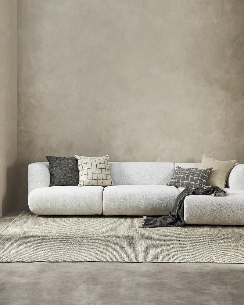 Complementary designer cushions by Baya in natural linen colours and black, styled on a white couch in a minimalist NZ living room.