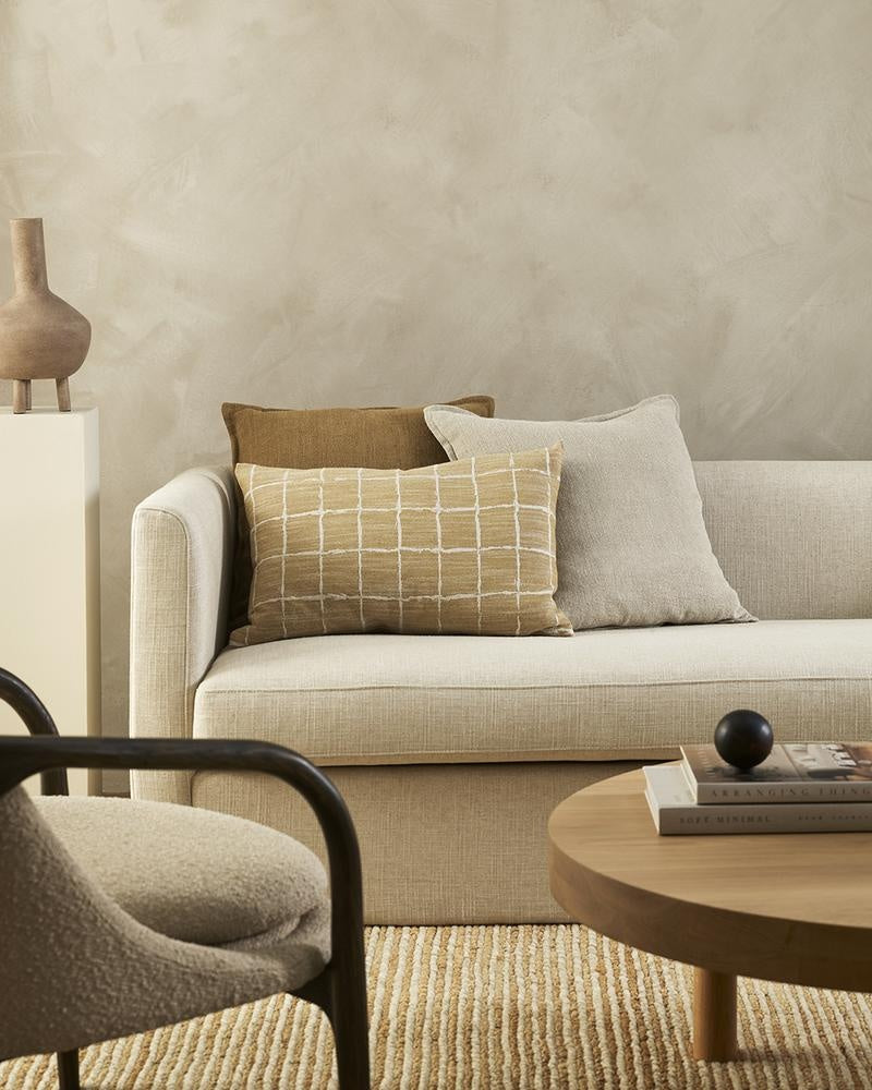 Baya's Johnson lumbar cushion - a stylish, geometric lumbar cushion featuring a grid pattern in a hand-painted style, and an earthy ochre  colour, styled with complementary cushions in a modern living room.