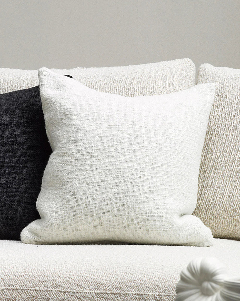 The Baya white textural cyprian cushion shown on a couch with a black contrast cushion