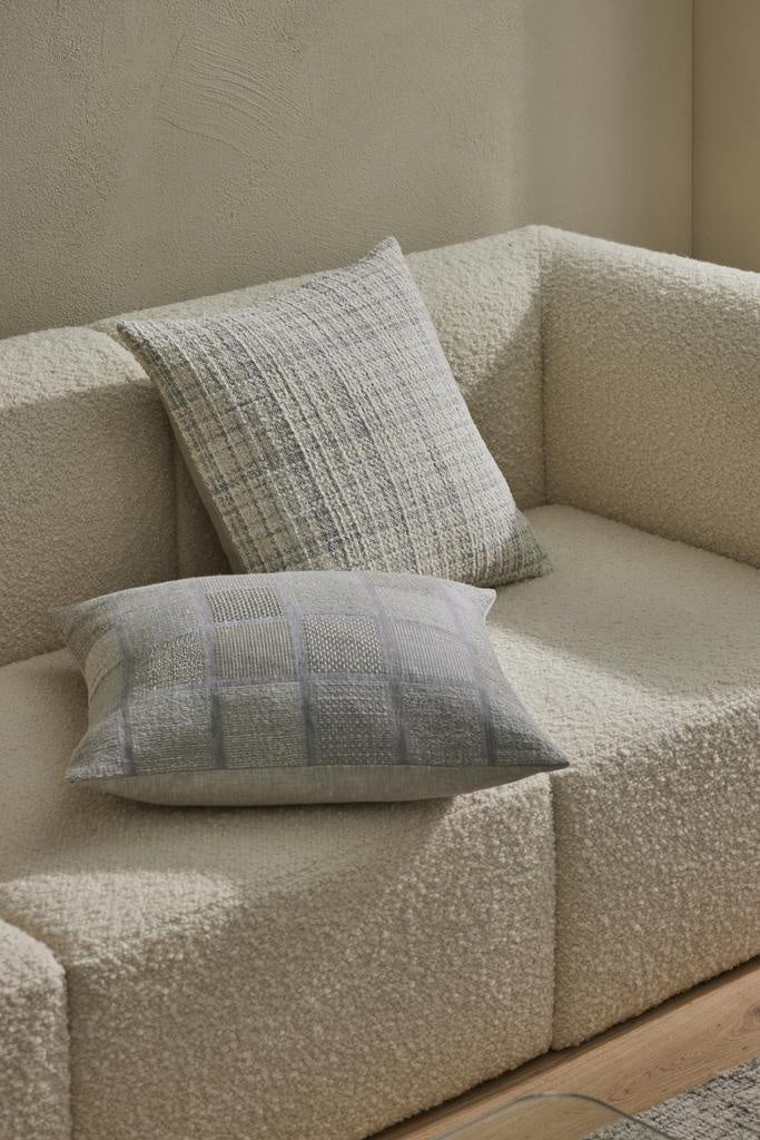 An on-trend woven cushion in white, alongside subtle beige and blue - the Tripoli Pearl by Weave, on a couch with a complementary cushion