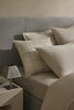 The Tripoli Pearl woven cushion by Weave Home, on a bed with beige bedding to add interest and style