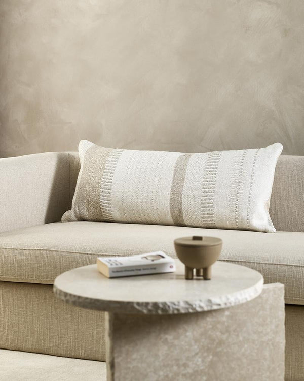 An extra-long lumbar cushion in white and beige - the Bettie by Baya -seen on a couch in a minimalist living room.