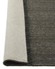 The 'Puglia' floor rug by Weave Home, in colour 'Pigeon" - a deep cool-toned brown, with edge folded up to reveal the backing.