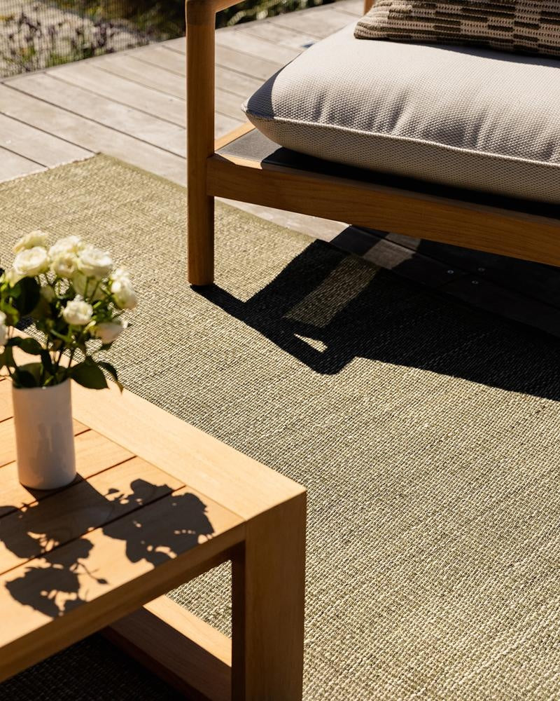 The olive green Lonsdale outdoor rug, by Baya, seen in the sun under stylish outdoor furniture