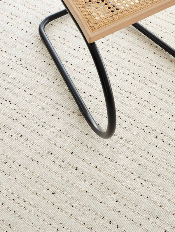 The Tribe Home Fritz floor rug , in colour ivory, seen from above - close up - with the corner of a chair showing for scale