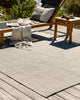 View of a stylish outdoor setting featuring the large, green Baya Lonsdale handwoven outdoor rug