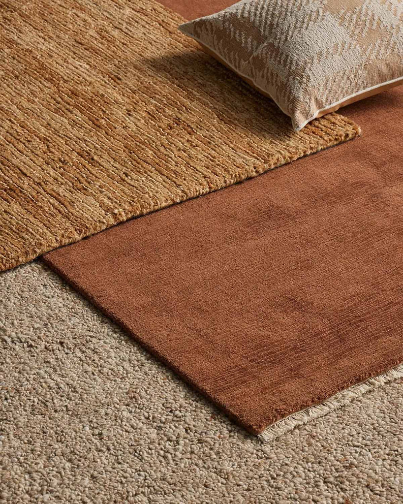A number of floor rugs in shades of brown, sienna and beige, with contrasting textures and materials, by Weave Home. 