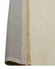 A corner of a linen floor rug in a soft cream tone with the edge flipped up to show the durable cotton backing and the underside of the fringed edge. 