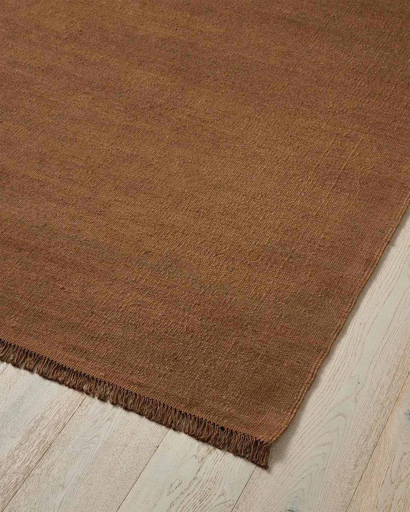 A corner image of a warm toffee brown floor rug handmade with 100% linen fibres. 