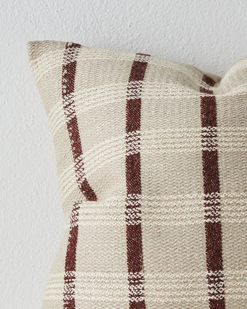 A close up of the Weave Home 'Marmaris' woven cushion featuring a dark brown stripe set against a contrasting white and neutrals.