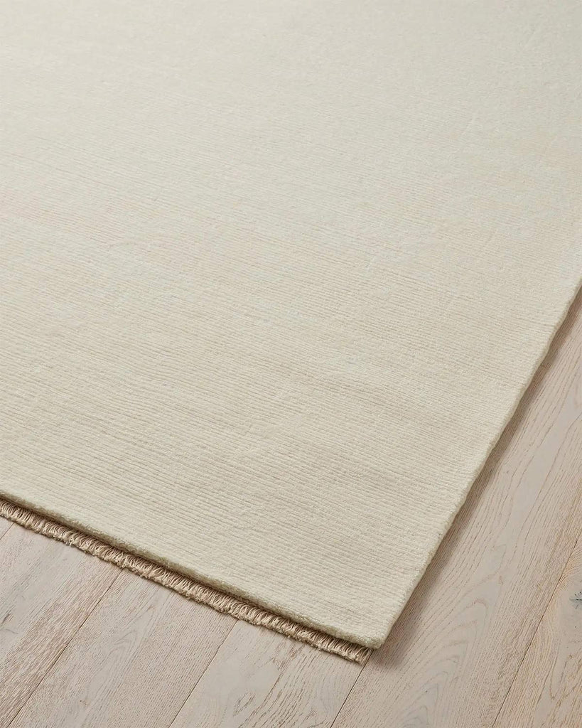 A corner of a soft cream ivory floor rug in 100% NZ wool with matching fringed edges. 