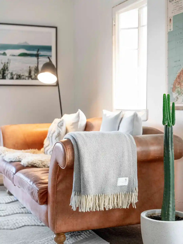 A soft, neutral grey wool throw, by Ruanui Station, in a pretty chevron pattern, shown draped over a couch