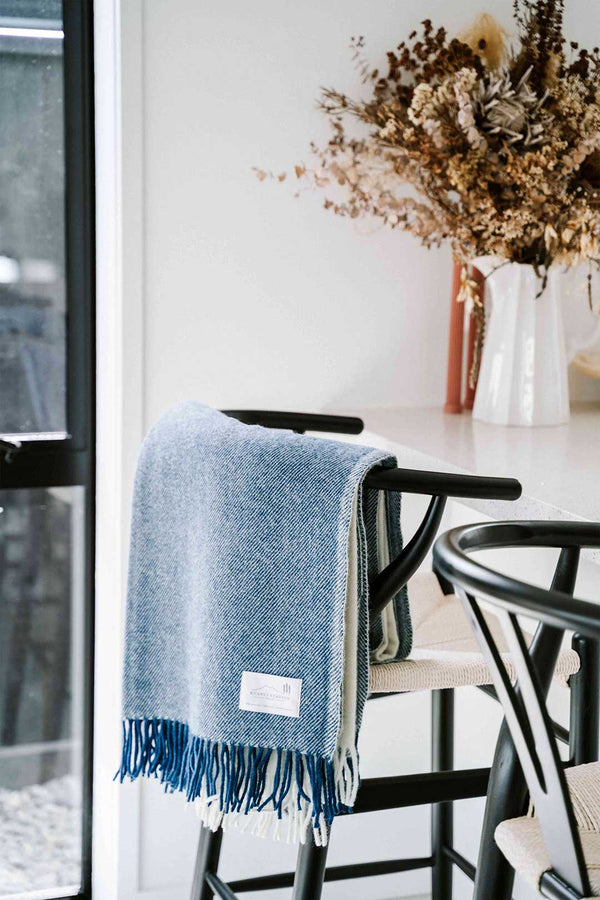 NZ wool throw blanket in blue nad white stripe, by Ruanui Station, seen hanging over the back of a chair