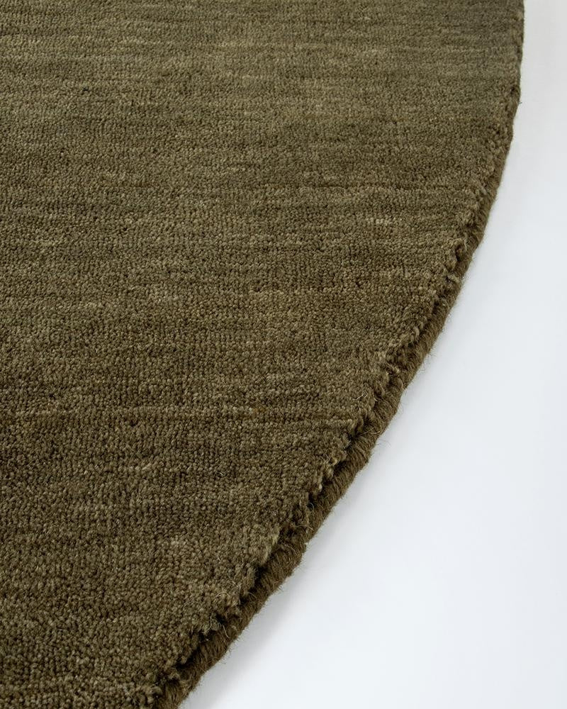 Edge close up of a round rug showing the wool pile, green colour and curve of the Sandringham Moss by Baya