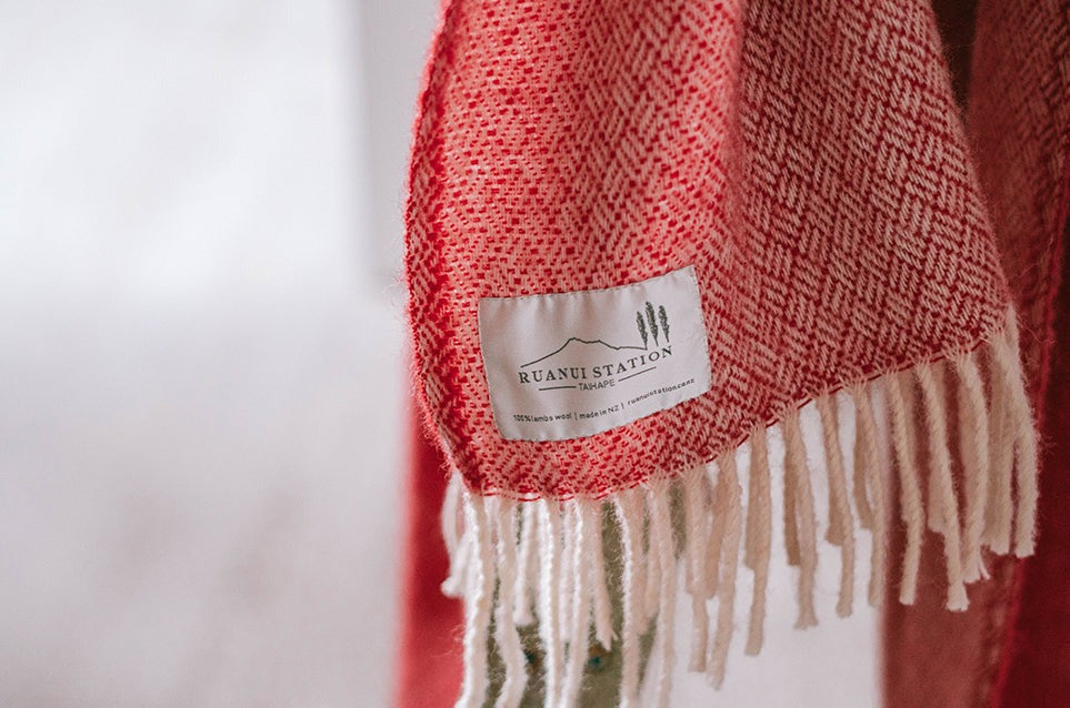 Close up of label and fringe detail of the pure wool NZ throw blanket by Ruanui Station, in vibrant 'Rakaia red'