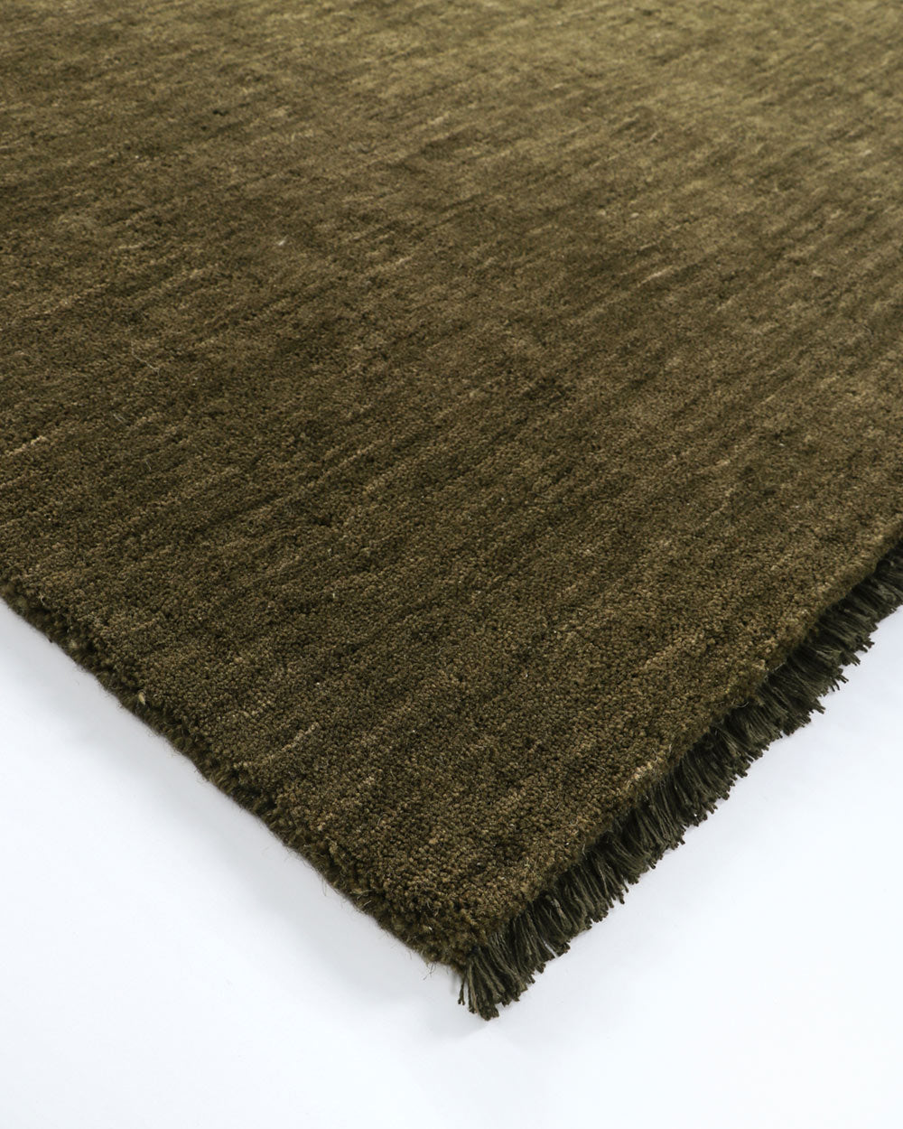 A corner image of a deep green floor rug with fringed edges by Baya. 