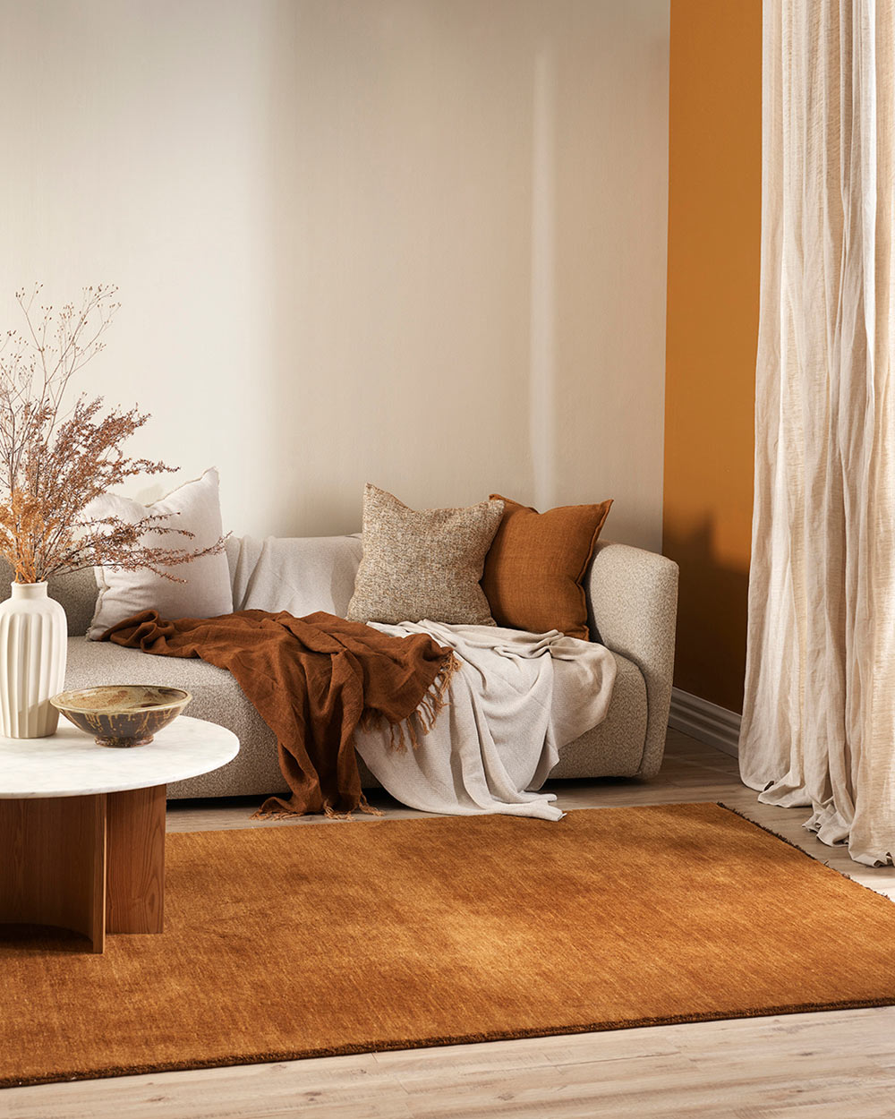 A cosy looking lounge in warm red-brown and cream tones with a soft brown floor rug by Baya. 