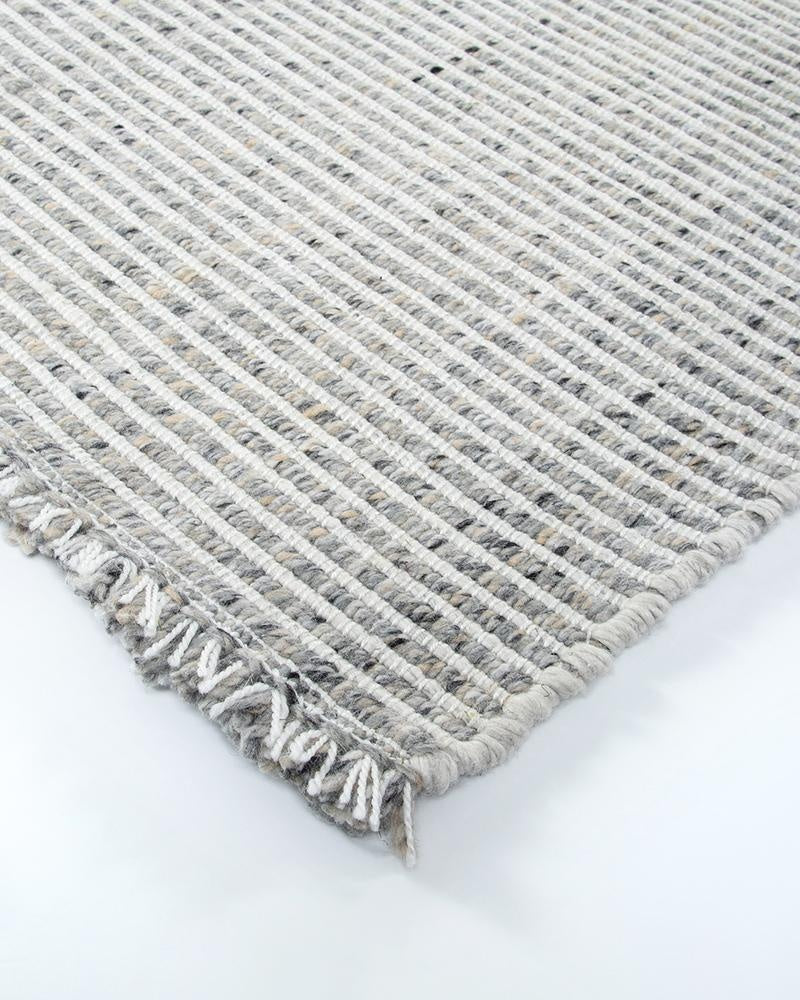 The Rhodes Slate Grey outdoor rug by Baya, seen at the corner showing a white and grey textural weave and fringe detail