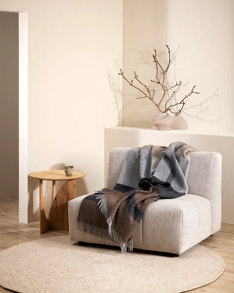 A neutral living room featuring the nz wool Brunswick throw balnket in soft greys, black and browns, draped over a cream chair