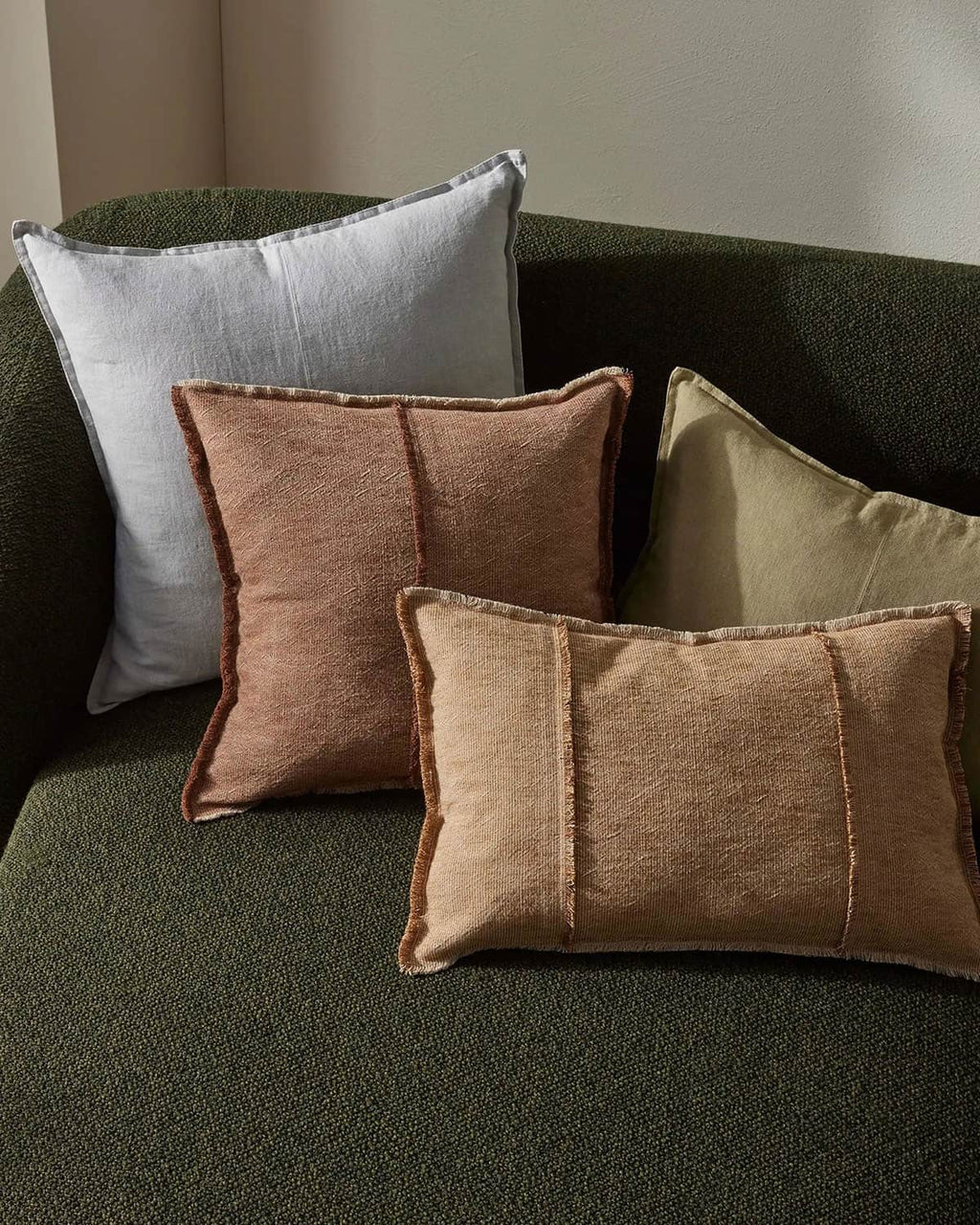 Four textured pillows in different colors on a green sofa.