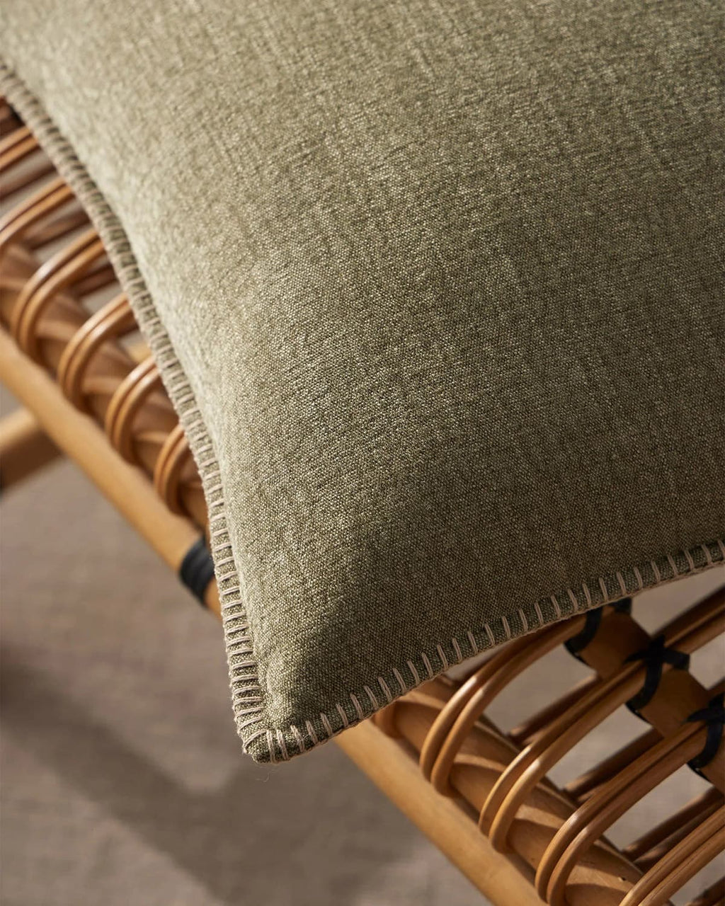 Close up of the elegant stitch detail on the Weave Home 'Alba Moss' cushion with cane chair underneath