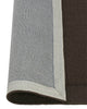 A Chocolate brown NZ wool floor rug with cut border, by Weave Home, with edge rolled to show underlay