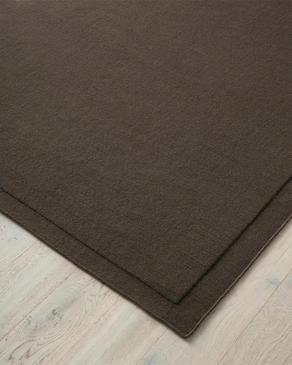 A close up corner of  Chocolate brown NZ wool floor rug with cut border, by Weave Home
