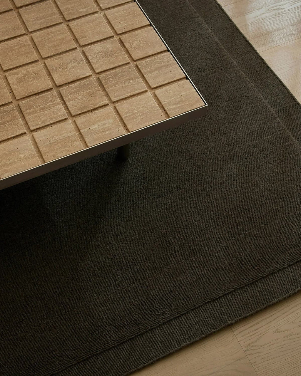 Close-up of a wooden table surface looking down on a chocolate brown wool floor rug