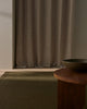 Brown curtain in a room with a wooden table and bowl and a designer wool rug