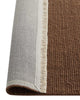Close-up of a brown rug corner with a white fringe, folded over to view the underside.