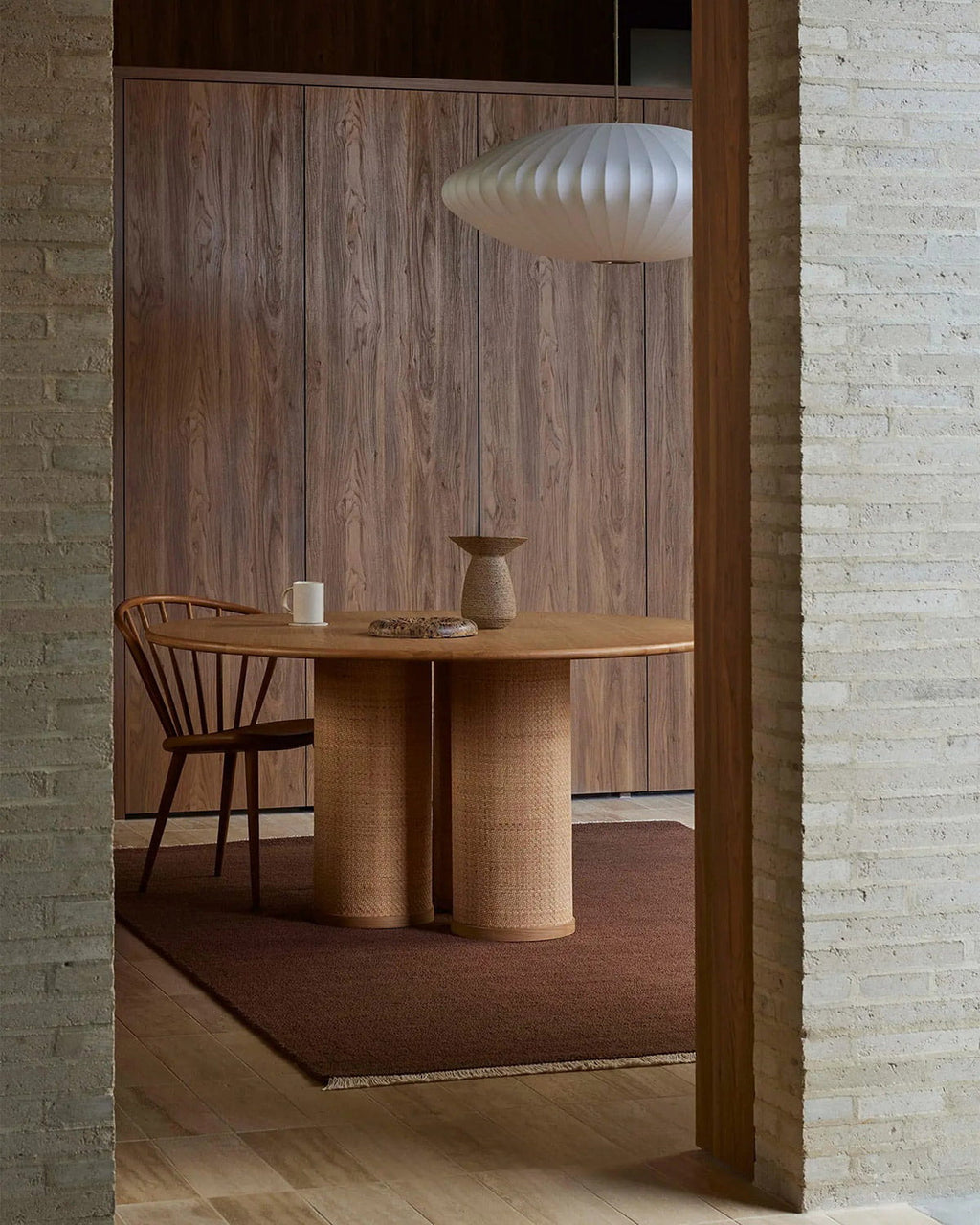 Dining area with wooden table and chair in a room with wooden walls and a textured brown floor rug.