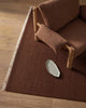 Brown textured rug with a wooden chair and a small white dish on a wooden floor.