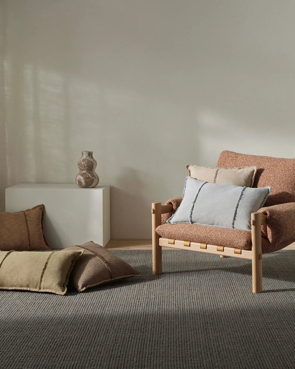 Modern living room with a brown armchair and decorative pillows against a neutral wall with a textural 100% wool gray rug.