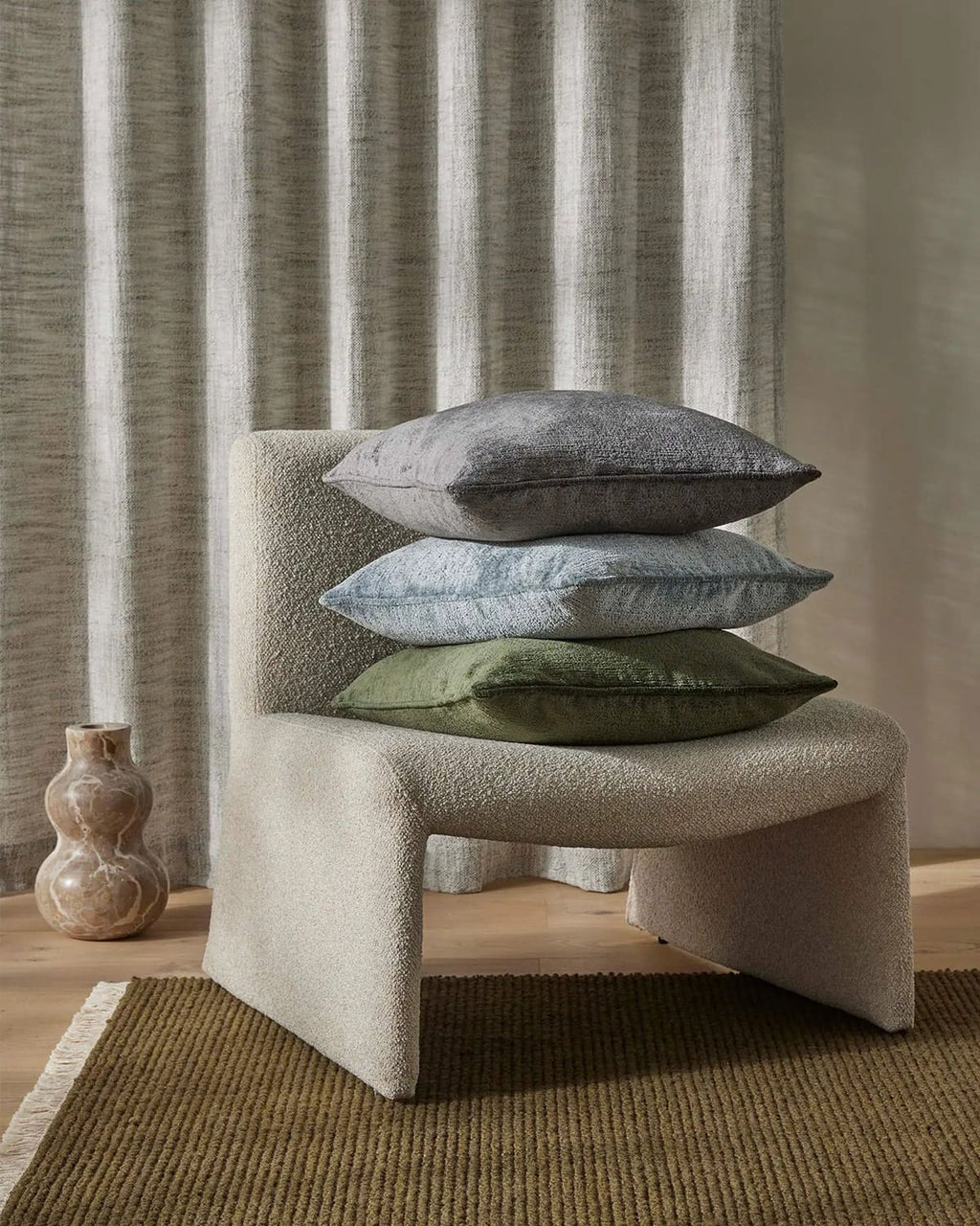 Chair with stacked cushions against a striped curtain on a green-brown textured floor rug.