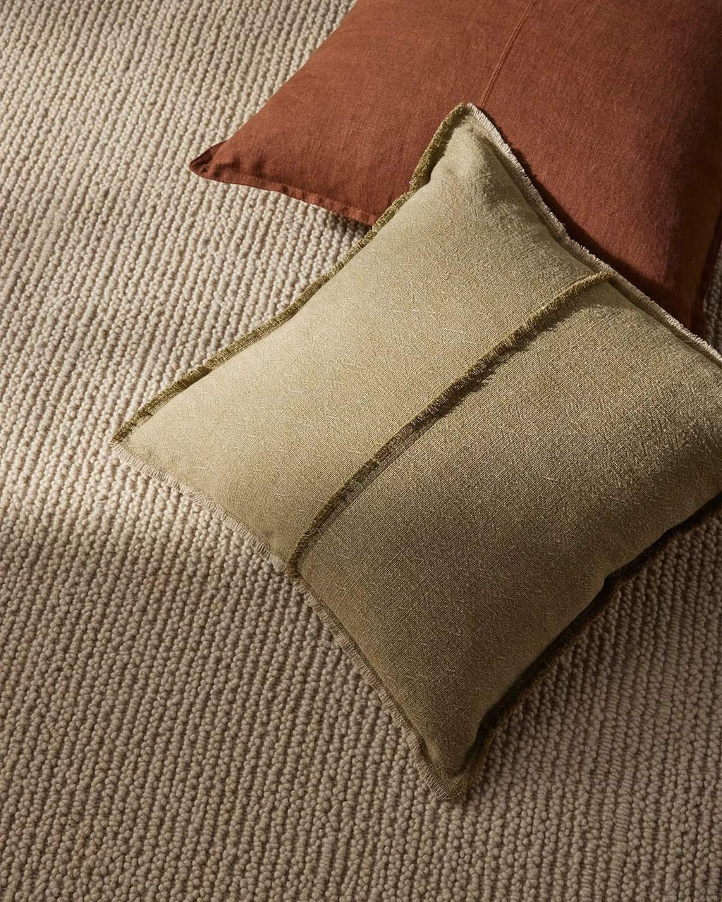Beige pillow with brown trim on a textured neutral beige floor rug