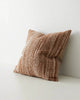 A textural, woven cushion in warm brown tones, seen at three quarter view