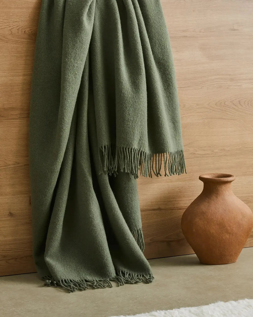 Weave Home wool throw blanket in colour 'juniper' - an on-trend muted green, seen draped, with fringe