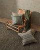 Weave Home wool throw blanket in colour 'juniper' - an on-trend muted green, draped over a chair with cushions