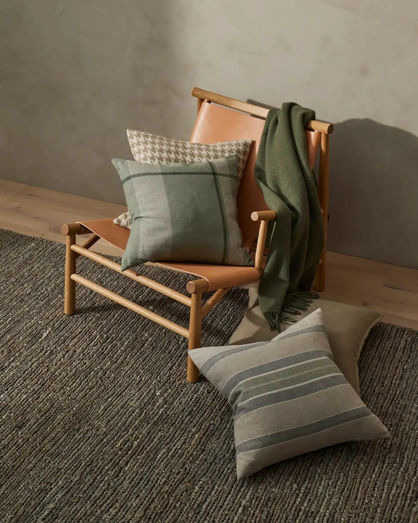 Weave Home wool throw blanket in colour 'juniper' - an on-trend muted green, draped over a chair with cushions