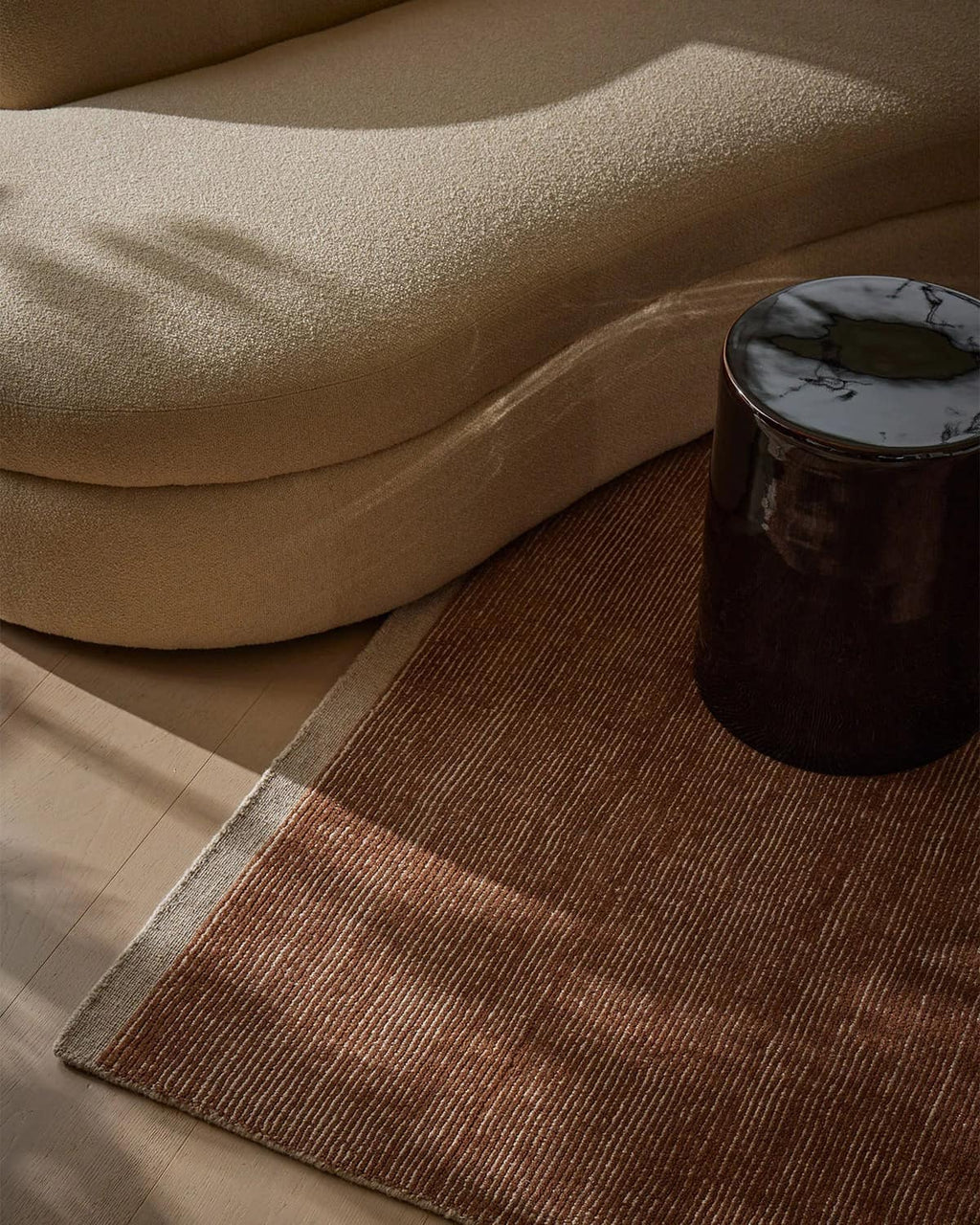 Weave Home NZ wool amber brown rug and sofa on a wooden floor.