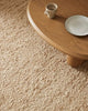 Close up view of the Henley floor rug in colour 'Ivory' showing its boucle texture and a table prop