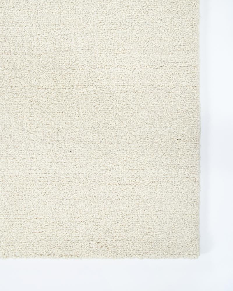 A light creamy-white wool floor rug with a boucle style weave, seen close up at a corner - the Dorset natural White by Baya