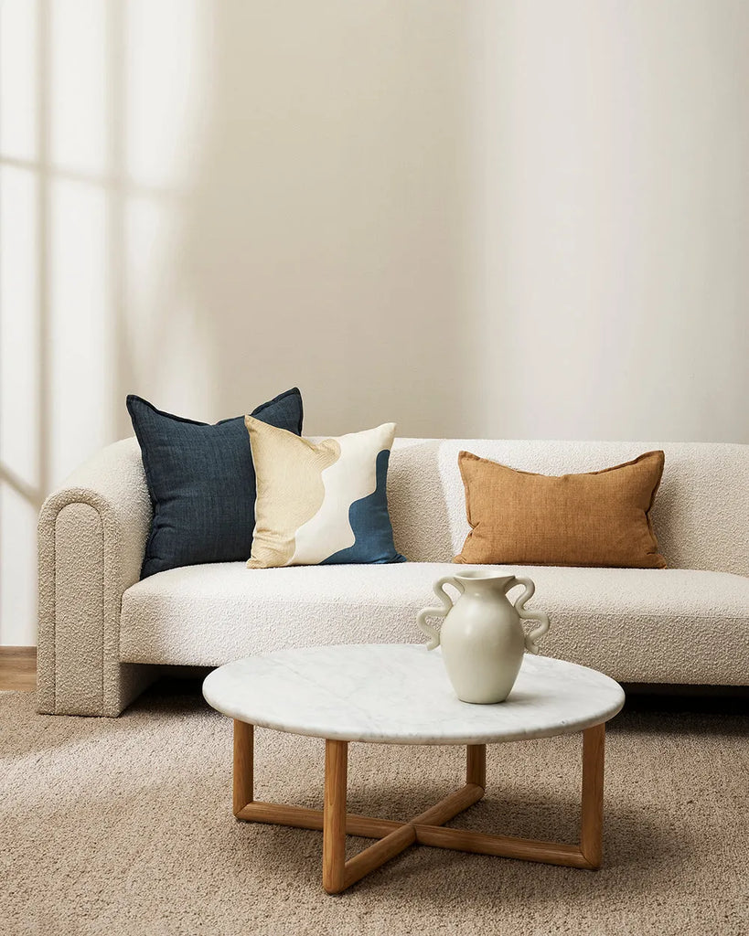 Baya linen lumbar cushion in a cumin brown, alongside contrasting blue on a  modern couch