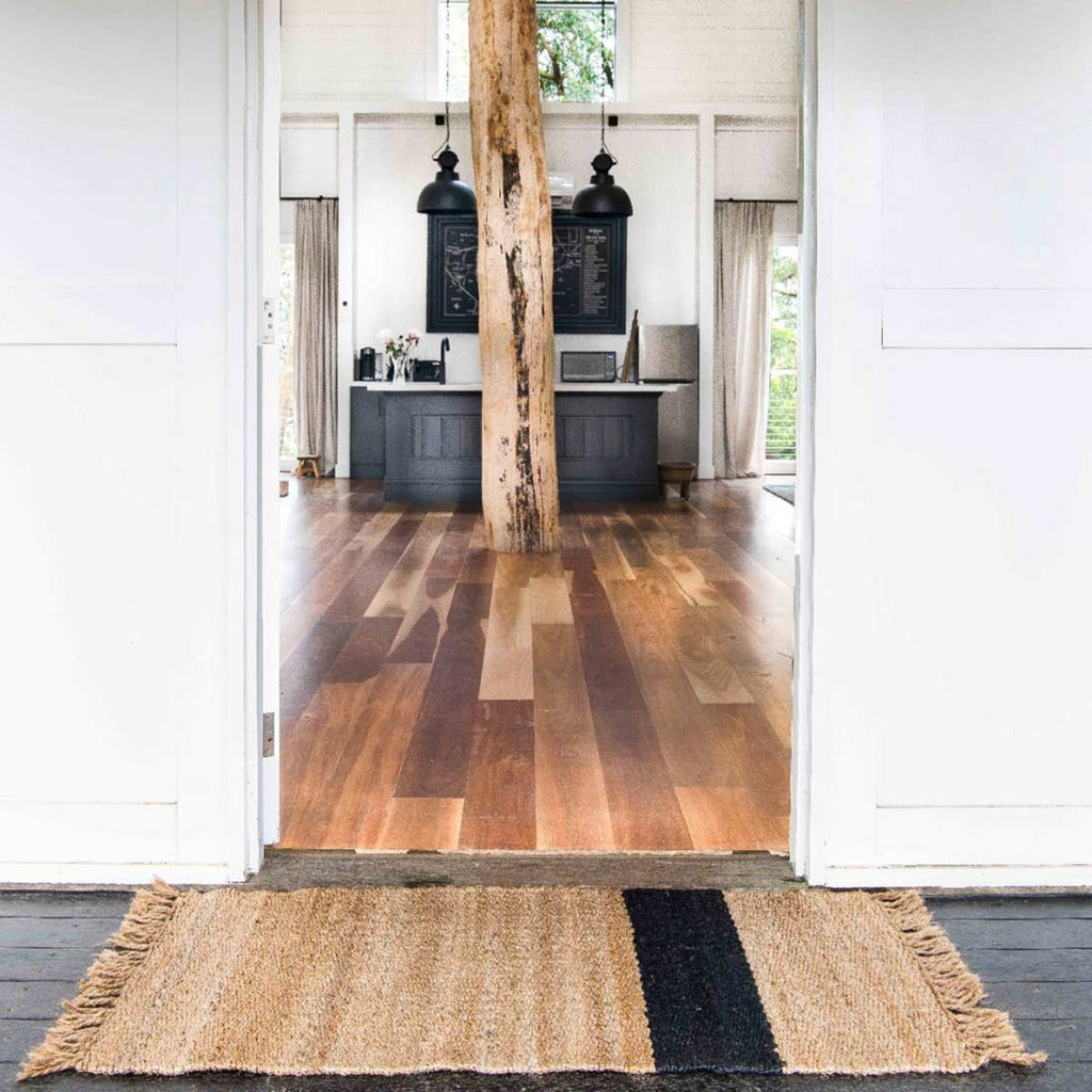 An entranceway with a natural brown toned jute doormat, with an asymmetrical black stripe. 