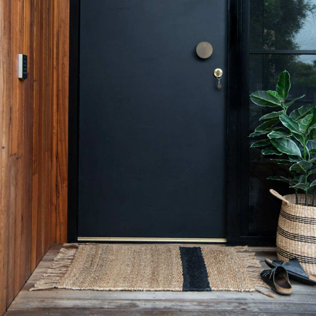 An entranceway with a doormat in 100% natural jute fibres, with a bold asymmetrical charcoal stripe and fringed edges. 