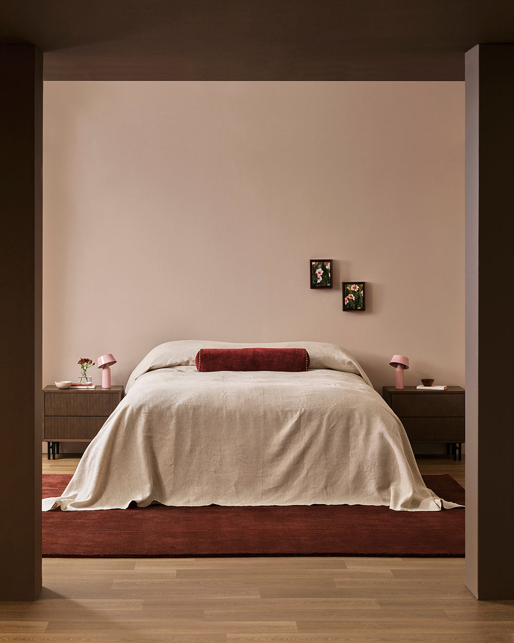 Baya Bastion NZ wool floor rug in Claret, styled under a bed with a linen throw, seen through a doorway in a bedroom.