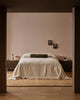 Baya Bastion NZ wool floor rug in Hazelnut, styled under a bed with a linen throw, seen through a doorway in a bedroom.