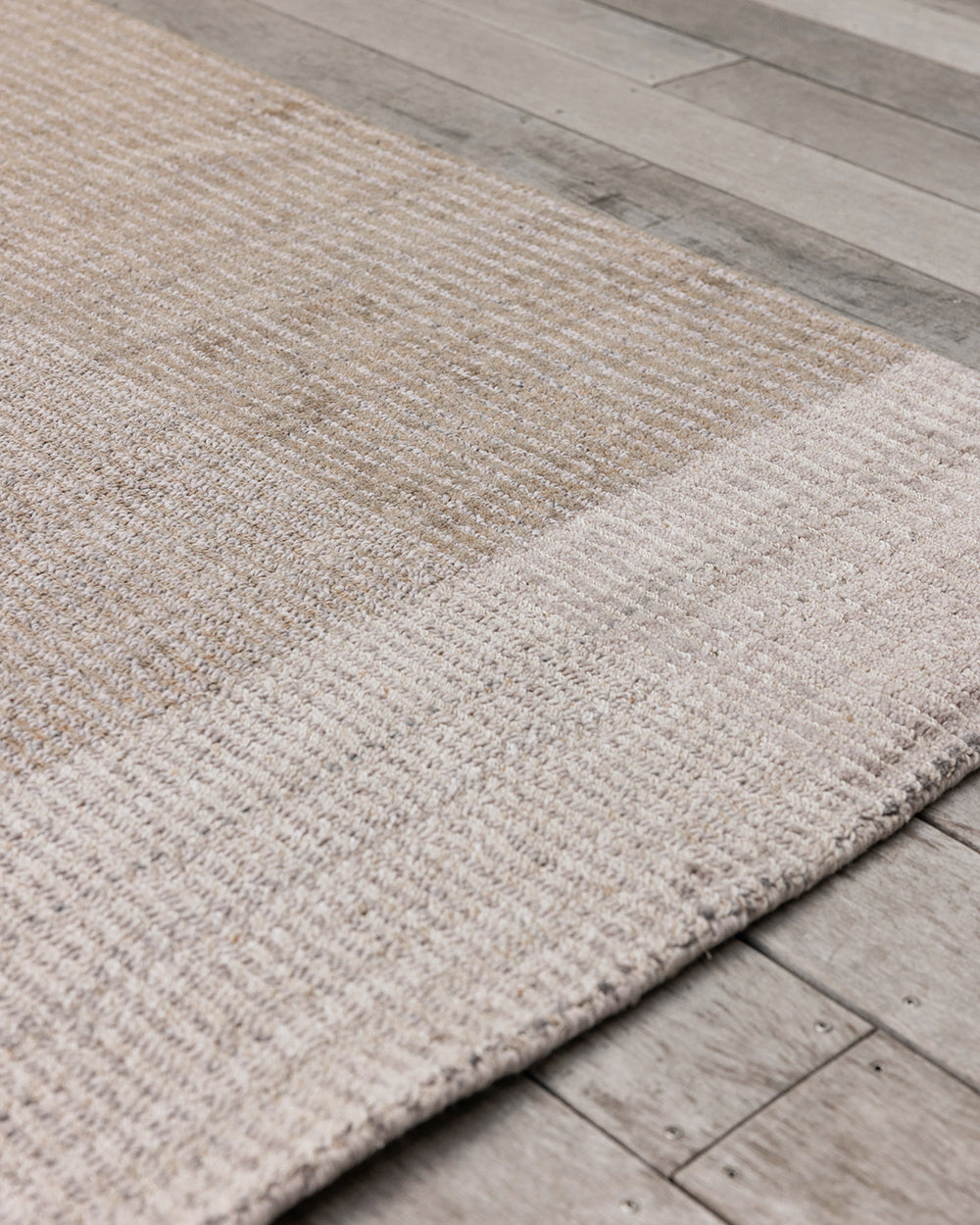 Baya Bedrock Indoor and Outdoor Floor Rug in Sand, close angled view on timber flooring showing the pale sand field meeting the lighter oatmeal striped border and edge binding.