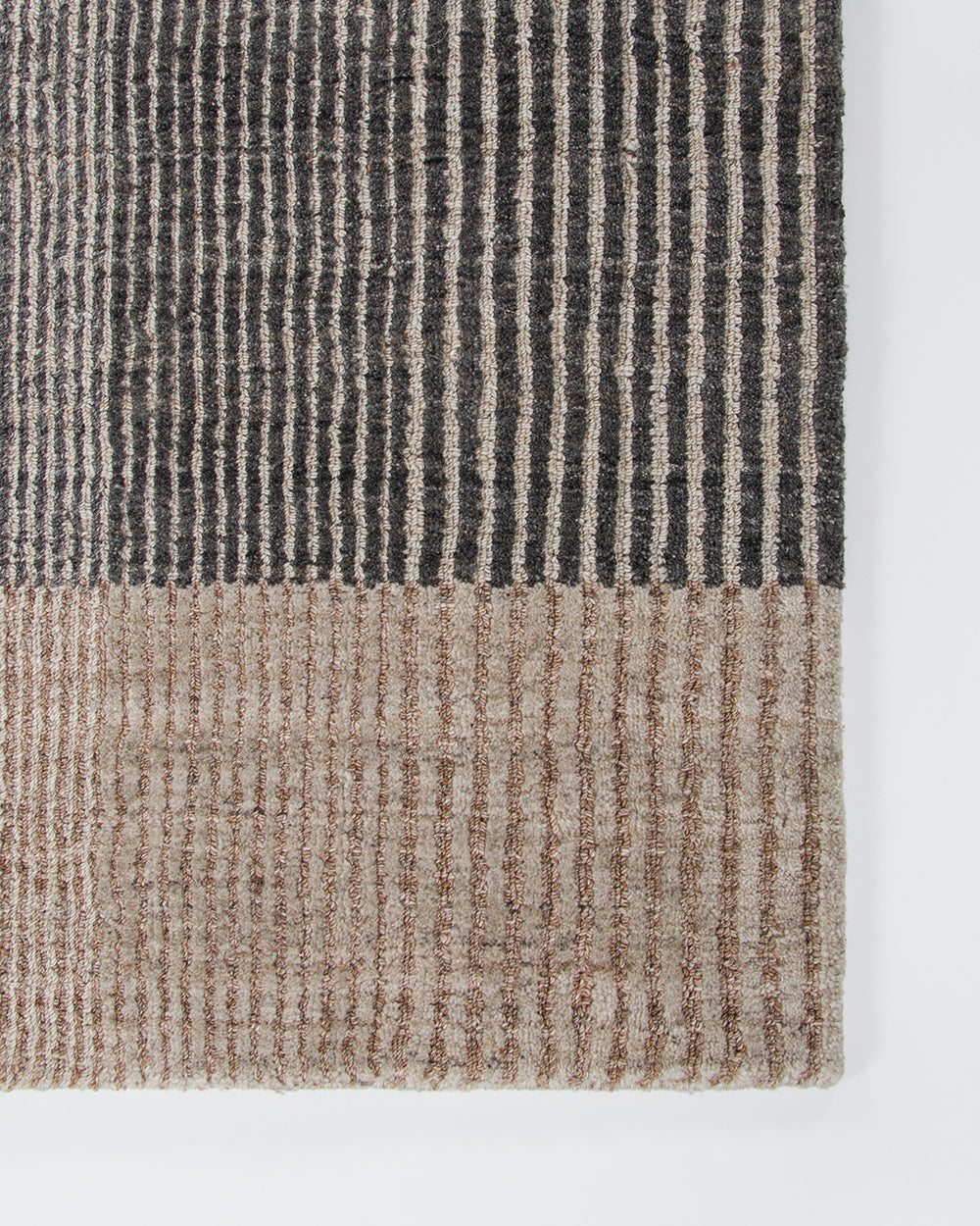 Baya Bedrock Indoor and Outdoor Floor Rug in Zinc, flat-lay corner detail on a white background showing the charcoal striped field meeting the sand-toned striped border and edge binding.